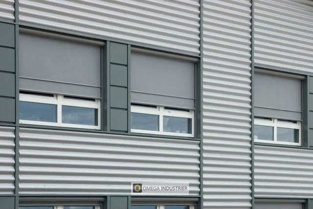 Gråe screens som dekker vinduer på bygg med metallfasade